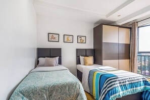 A hotel room with two single beds, a large window with curtains, and three framed pictures on the wall. - Urban Oasis (Nairobi)