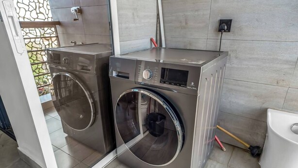 Un moderno lavadero con dos lavadoras de carga frontal de acero inoxidable, un pequeño panel de control y un inodoro blanco.