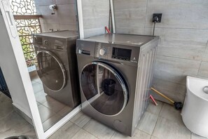 A modern laundry room with two stainless steel front-loading washing machines, a small control panel, and a white toilet. - Urban Oasis (Nairobi)