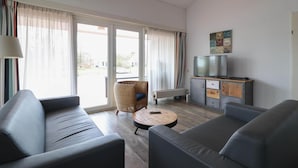Una sala de estar moderna con un sofá, una mesita redonda y un televisor sobre un mueble.
