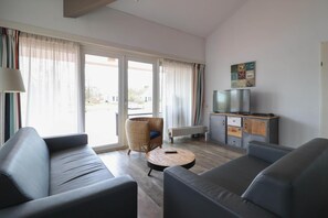 Ein modernes Wohnzimmer mit einer Couch, einem kleinen runden Tisch und einem Fernseher auf einem Schrank.