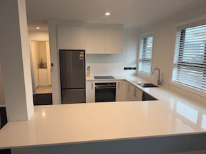 Una cocina moderna con armarios blancos, un refrigerador de acero inoxidable, un horno integrado y una encimera amplia.