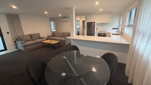 A modern living space with a sofa set, a coffee table, a glass dining table, and a kitchen area with a refrigerator and sink. - Central Apartments Rotorua (Rotorua)