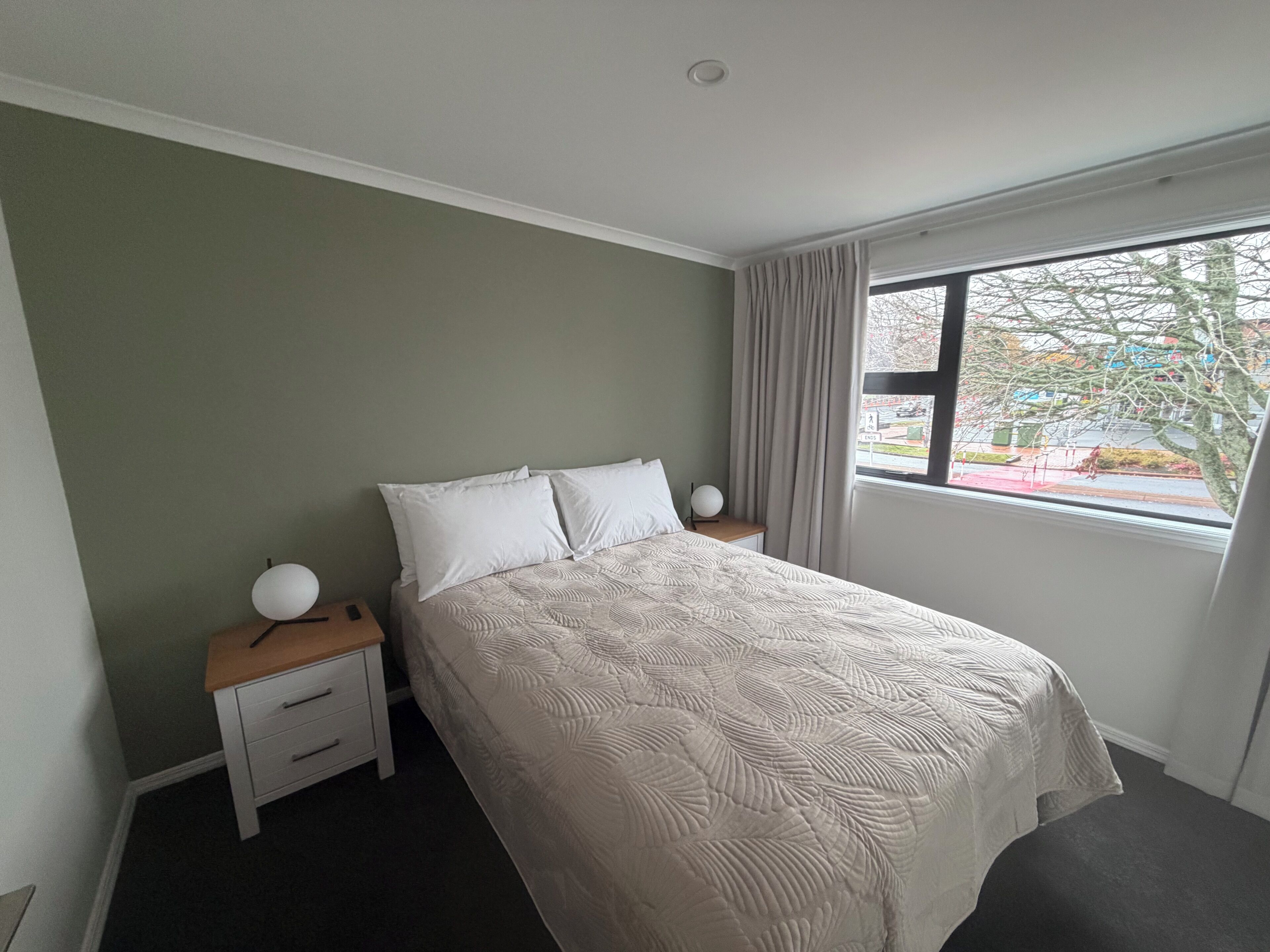 Un dormitorio con cama, mesitas de noche, una ventana y vistas al exterior.
