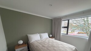 A bedroom with a bed, bedside tables, a window, and a view of the outside. - Central Apartments Rotorua (Rotorua)
