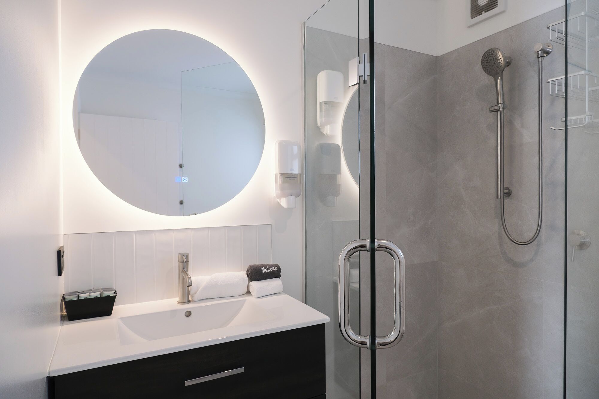 A modern bathroom with a round mirror, a glass-enclosed shower, and a vanity with a sink.