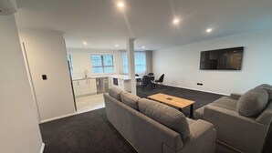 A modern living room with a grey sofa set, a wooden coffee table, and a dining area with a table and chairs. - Central Apartments Rotorua (Rotorua)