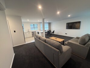 A modern living room with a grey sofa set, a wooden coffee table, and a dining area with a table and chairs.