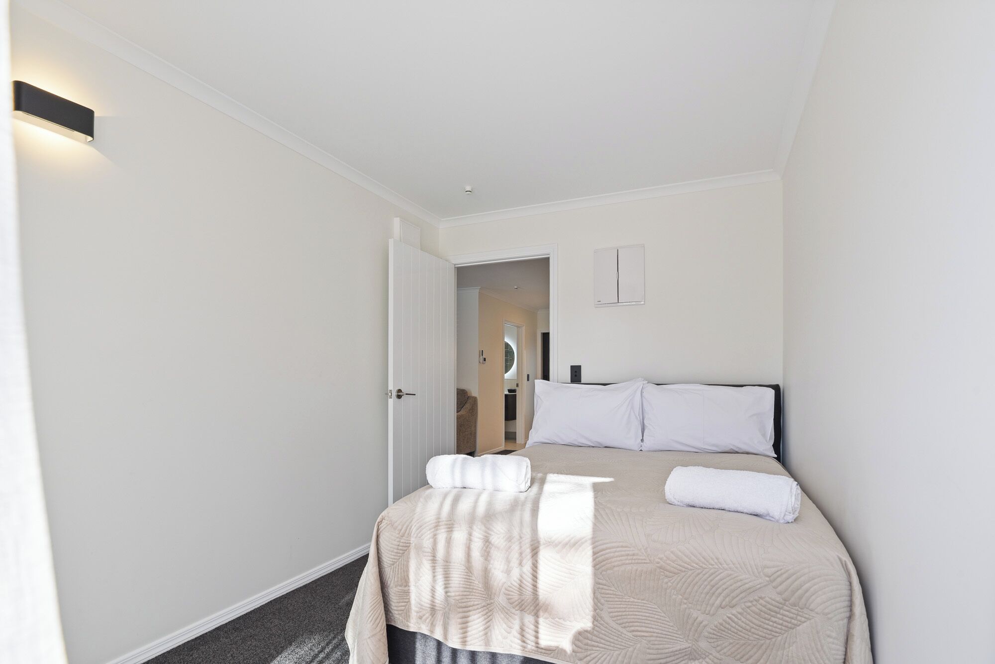 A hotel room with a bed, a door, and a wall-mounted light fixture.