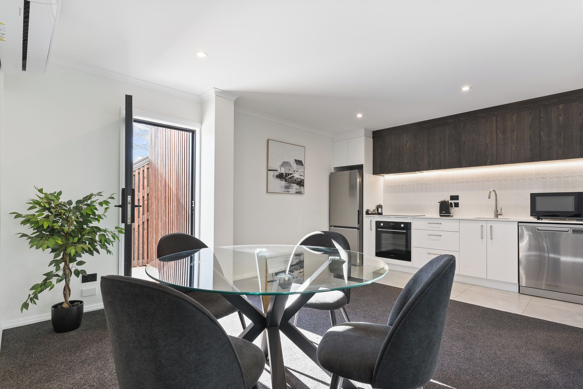 A modern kitchen with stainless steel appliances, a glass dining table, and a potted plant.