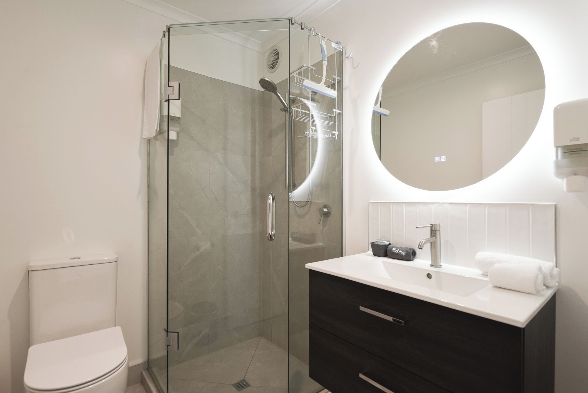 A modern bathroom with a glass-enclosed shower, a white toilet, and a vanity with a mirror.