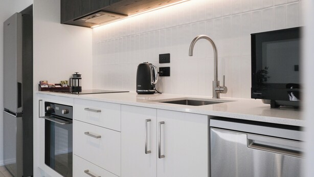 A modern kitchen with stainless steel appliances, a black coffee maker, and a built-in TV. - Central Apartments Rotorua (Rotorua)