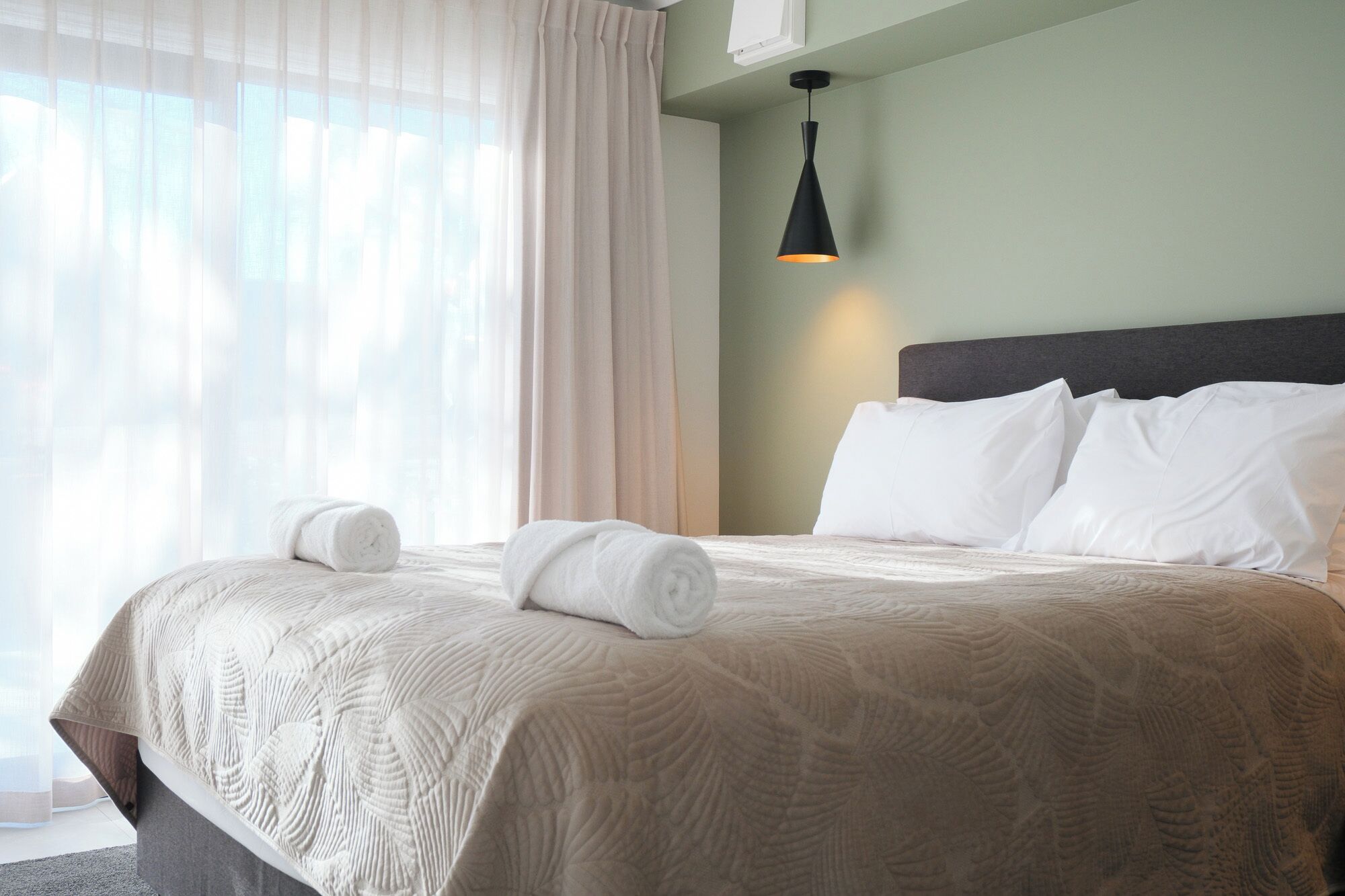 A hotel room with a bed, white pillows, and a black pendant light.