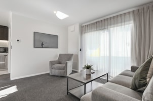 A modern living room with a grey sofa, a matching armchair, a coffee table, and a large window with sheer curtains.
