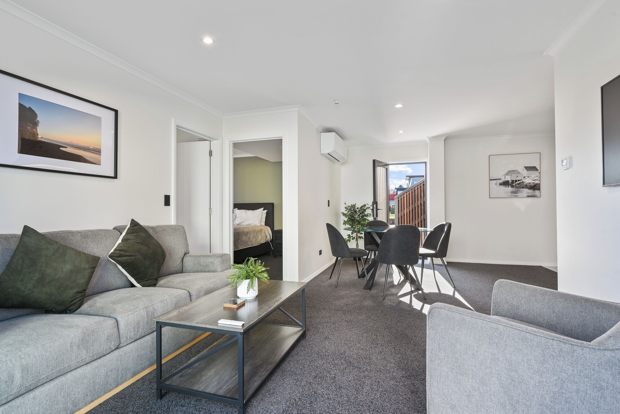A modern living room with a grey sofa, a coffee table, and a dining area with chairs and a table.