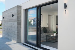 Een modern gebouw met een glazen deur, een betonnen gevel en zichtbare inrichting met een bank en een salontafel.