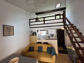 A compact living space with a sofa, a dining table, a kitchenette, and a wooden staircase.