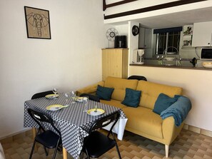 Ein Essbereich mit Tisch für vier Personen, einer Couch und einer Küche im Hintergrund.