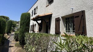 Un edifici amb façana blanca, una pèrgola de fusta i una finestra amb persianes.