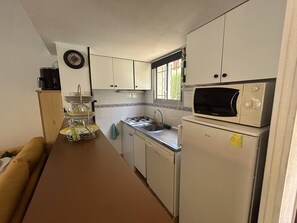 Uma cozinha compacta com armários brancos, micro-ondas, fogão e pia.