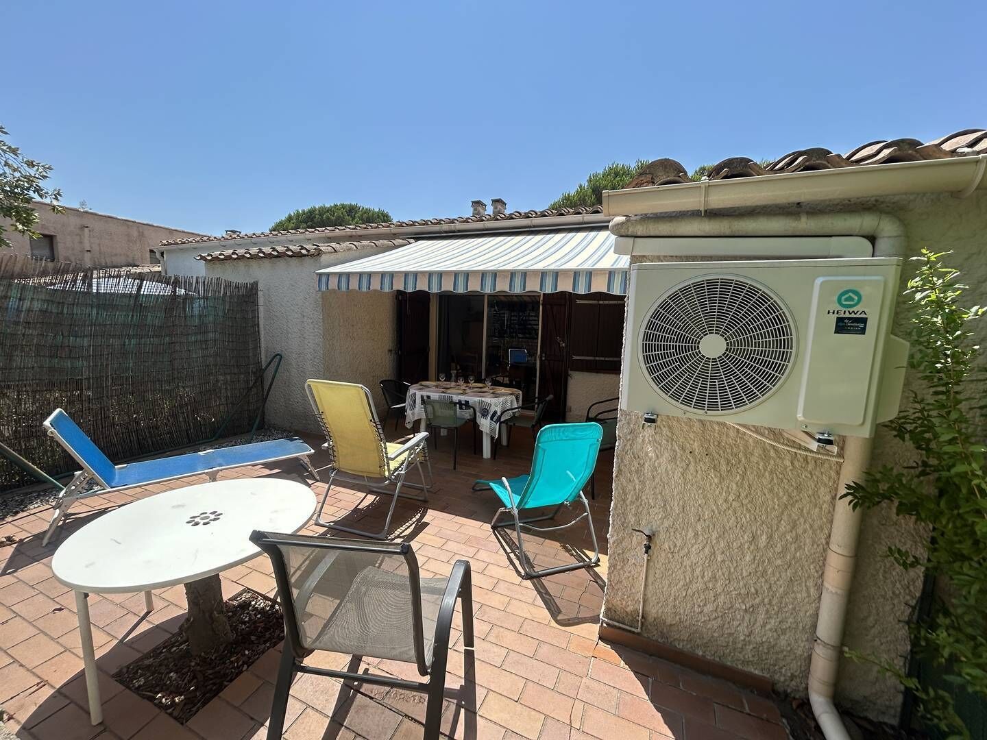 An outdoor patio with a table and chairs, an air conditioning unit, and a covered seating area.