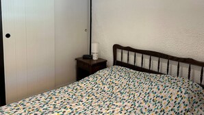Un dormitori amb un llit, una tauleta de nit, una porta blanca i un quadre penjat a la paret.