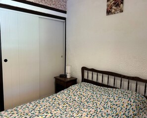 A bedroom with a bed, a nightstand, a white door, and a wall-mounted picture. - Lovely 3-room semi-detached villa with mezzanine in Mont Saint-Martin, Cap d'Agde. (LE CAP D AGDE)