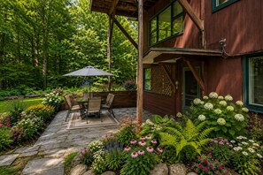 Een houten huis met een terras, tuinmeubilair en diverse bloemen.