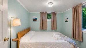 A neatly made bed with a wooden headboard, a bedside lamp, and two paintings on the wall. - First Floor Retreat | Minutes to Stowe Mountain (Stowe)