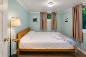 Ein ordentlich bezogenes Bett mit einem Holzkopfende, einer Nachttischlampe und zwei Bildern an der Wand.