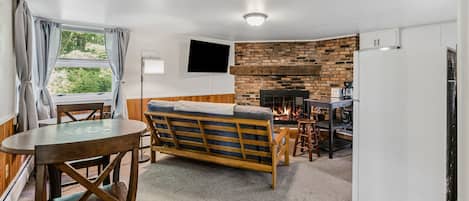 A compact living space with a sofa, a dining table, a kitchen area with a brick wall, and a TV mounted on the wall.