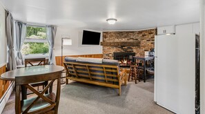 Un espacio habitable funcional con sofá, mesa de comedor, área de cocina con pared de ladrillo y televisor montado en la pared.
