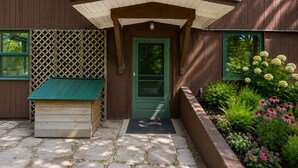 A wooden house with a green door, a small porch with a bench, and a garden with various plants and flowers. - First Floor Retreat | Minutes to Stowe Mountain (Stowe)