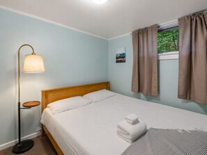Een slaapkamer met een enkel bed, een nachtkastje, een vloerlamp en een raam met gordijnen.