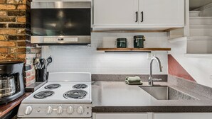 A kitchen with white cabinets, a stainless steel range hood, a built-in oven, a sink with a faucet, and a coffee maker. - First Floor Retreat | Minutes to Stowe Mountain (Stowe)