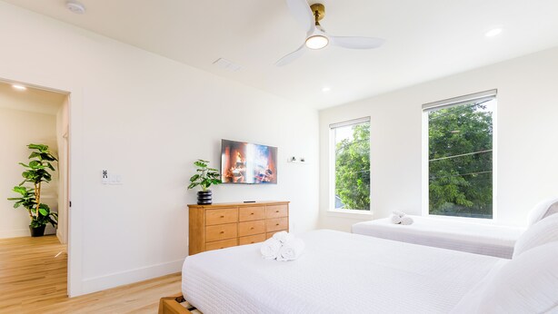 Una camera da letto con un letto, una cassettiera, una ventola a soffitto e una finestra vista alberi.
