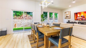 Un'area pranzo moderna con un tavolo di legno, sedie e vista su un giardino tramite ampie finestre.