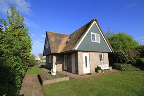 A traditional house with a thatched roof, a small front porch, and a bench. - Deluxe Beach Villa With Garden (Makkum)