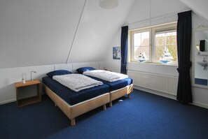 Un dormitorio con dos camas, una ventana con cortinas, un radiador y una mesita de noche con lámpara.