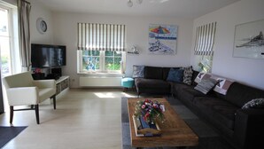 Una sala de estar con un sofá, una mesa de centro con flores, un televisor y una ventana con cortinas.