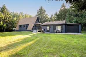 A two-story house with a sloped roof, a covered porch, and a garage. - Secluded A-Frame on 10 Acres | At the Pines (Fennville)