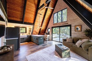 A spacious loft with a kitchen, dining area, and living room, featuring wooden beams, large windows, and a cozy seating area. - Secluded A-Frame on 10 Acres | At the Pines (Fennville)