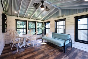 A room with a dining table, chairs, a sofa, and large windows. - Secluded A-Frame on 10 Acres | At the Pines (Fennville)