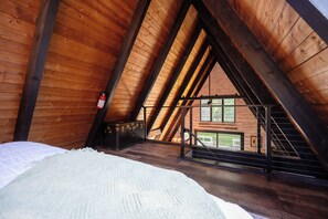 A high-ceilinged wooden room with a sloped roof, a bed, and a window overlooking a balcony. - Secluded A-Frame on 10 Acres | At the Pines (Fennville)