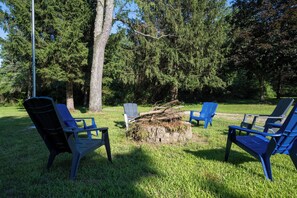 A grassy outdoor area with four blue Adirondack chairs arranged in a semi-circle around a stone fire pit. - Secluded A-Frame on 10 Acres | At the Pines (Fennville)