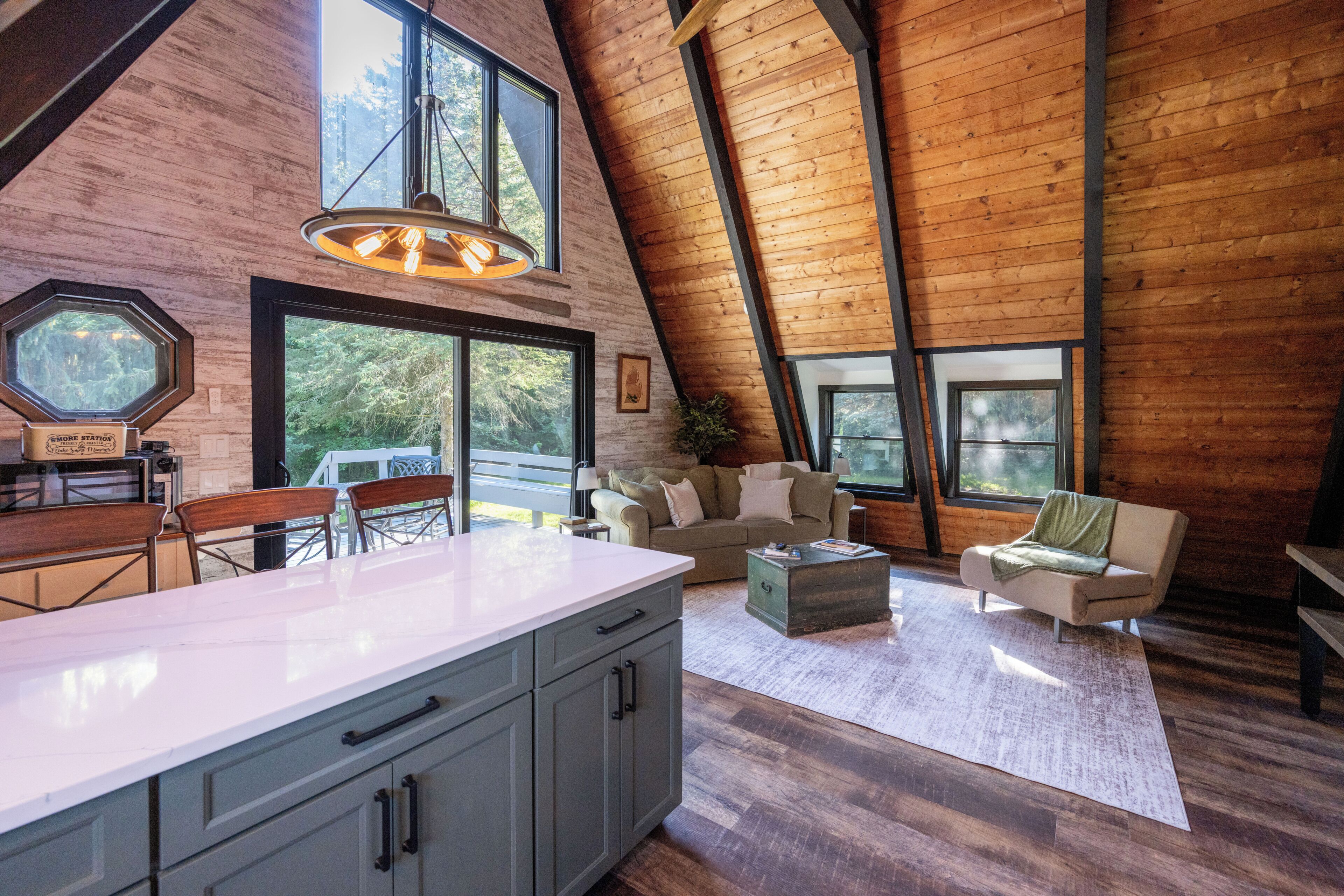 A spacious loft with a high ceiling, large windows, a kitchen area, and a seating area with a view of the outdoors.