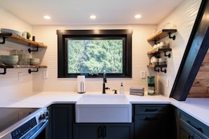 A modern kitchen with a built-in window, white countertops, and black cabinetry. - Secluded A-Frame on 10 Acres | At the Pines (Fennville)