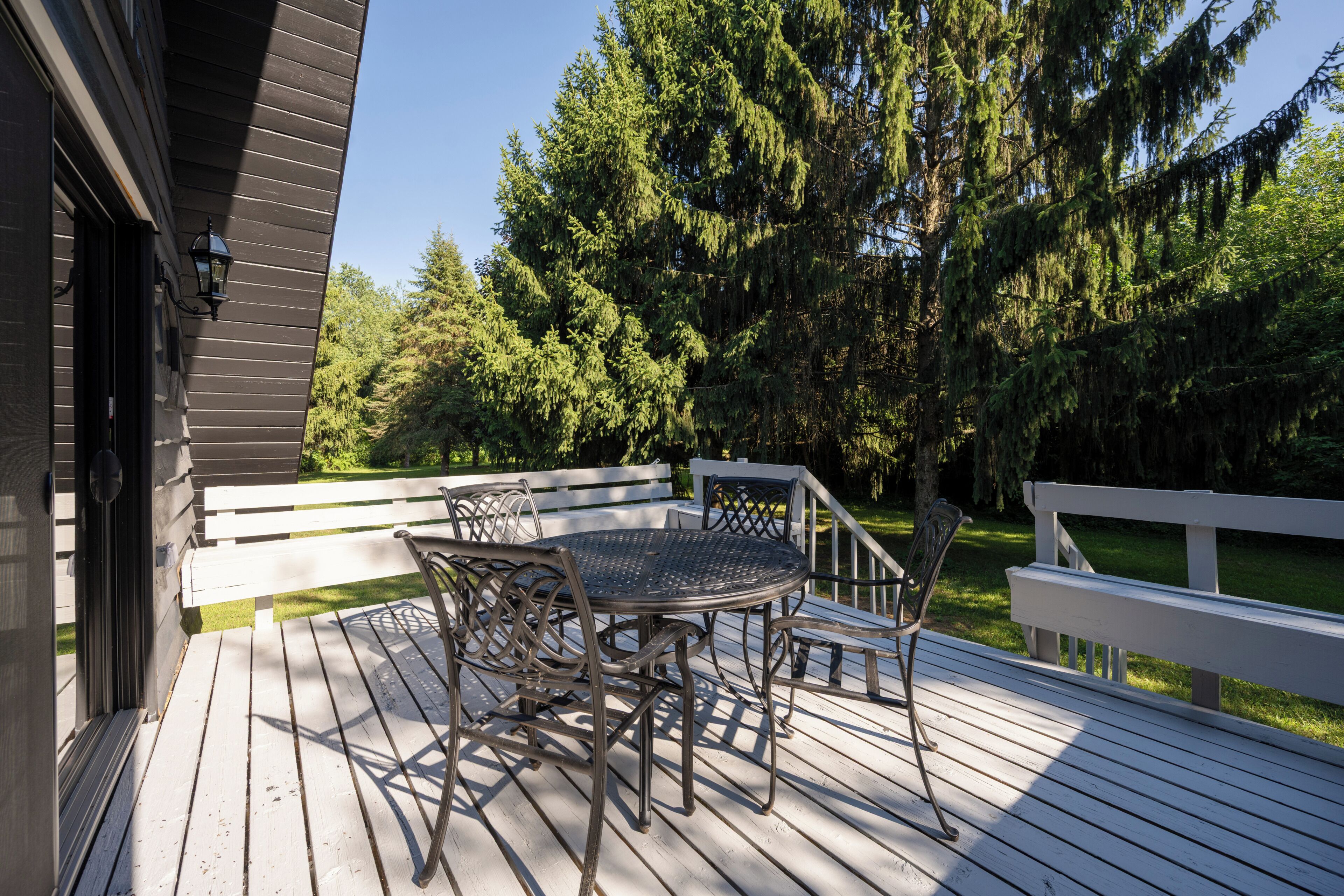 A wooden deck with a metal table and chairs, surrounded by trees.