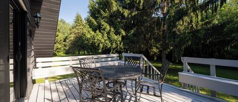 A wooden deck with a metal table and chairs, surrounded by trees.