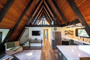 A spacious attic bedroom with a sloped ceiling, a large window, and a view of the outdoors. - Secluded A-Frame on 10 Acres | At the Pines (Fennville)